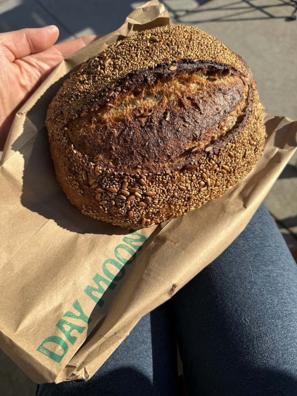 A sesame sourdough loaf in a Day Moon paper bag